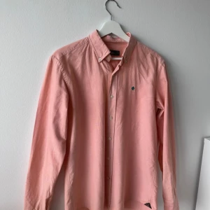 Morris skjorta  - Snygg skjorta från Morris i storlek M med klassisk button-down krage och broderad logga på bröstet. aprikos/rosa.Skjortan har långa ärmar och knappar framtill. Skicka prisförslag!!!