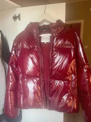 Vinröd pufferjacka från Tommy Hilfiger - Säljer en glansig vinröd pufferjacka från Tommy Hilfiger med huva och dragkedja framtill. Nypris: 2200kr 💕