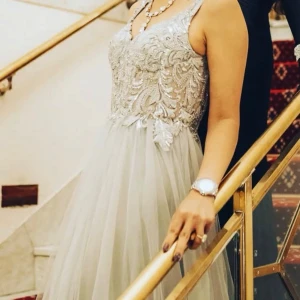 Silverfärgad långklänning med paljetter - Säljer en elegant långklänning i silverton med glittrande paljetter och broderade detaljer på livet. Klänningen har breda axelband och ett skirt, flödande tyg i kjolen som ger en lyxig känsla. Dragkedja i ryggen för enkel påklädning. Perfekt för bal eller nyår.