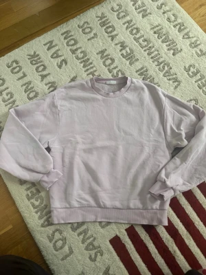 Ljusrosa sweatshirt från Gina Tricot - En enkel och snygg ljusrosa sweatshirt från Gina Tricot, basically basics-kollektionen. Tröjan har rund hals, ribbade muddar vid ärmslut och nederkant samt långärmad passform. Perfekt för chill dagar och enkel att matcha med jeans eller mjukisbyxor.