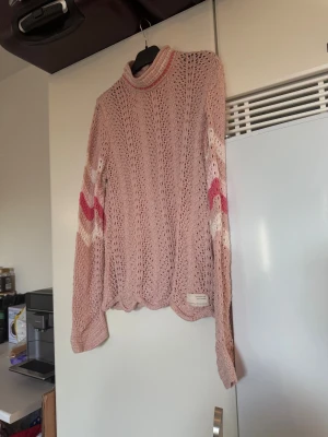 Rosa stickad polotröja Odd Molly - Säljer en ljusrosa stickad polotröja från Odd Molly med lång ärm och snygga vågiga mönster i vitt och rosa på ärmar och rygg. Tröjan har en hög krage med rosa detalj och är genombruten i materialet för en cool look. Storlek 1 som enligt deras storleksguide motsvarar en S.  Mycket fint skick, jag hittar inga synliga anmärkningar eller defekter. 