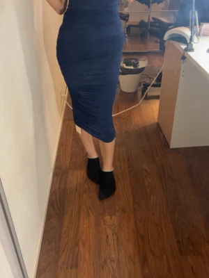 Marinblå omlottklänning med v-ringning - Säljer en marinblå långklänning med omlott och v-ringad hals. Klänningen har en figurnära passform och är gjord i ett stretchigt material som framhäver siluetten. Perfekt för dig som gillar stilrena och eleganta plagg.