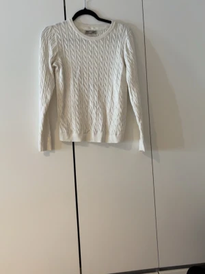 Vit kabelstickad tröja Basic You S - Säljer en vit kabelstickad tröja från Basic You i storlek S. Tröjan är gjord av ekologisk bomull och har rund hals samt långa ärmar. Perfekt för dig som gillar klassisk stil med twist. Snyggt mönster och mjukt material.