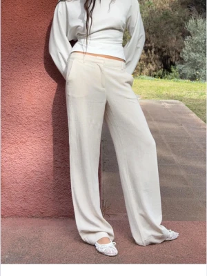 Beiga linnebyxor från Nelly EU 40 - Snygga och luftiga linnebyxor från Nelly i beige färg. Byxorna har en rak och wide passform med midwaist och klassisk kostymstil. Perfekta för dig som gillar en chill och stilren look. Materialet är linne som ger en skön känsla och naturlig struktur. Dessa byxor är aldrig använda o lappen fins kvar. Kan ta fler bilder om de efterfrågas