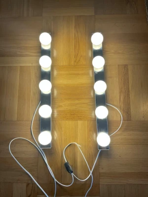 Sminkspegelbelysning med LED-lampor - Säljer ett set med sminkspegelbelysning bestående av två raka metallister med fem runda vita LED-lampor på varje. Lamporna är kopplade med vit sladd och har en svart strömbrytare. Perfekt för att få jämnt ljus när du sminkar dig.
