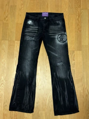 Svarta Chainway Lukamachain jeans - Unika svarta jeans från Lukamachain med grå sprayade detaljer och slitningar. Byxorna har ett stort tryckt logomärke på fickan bak och framtill, samt raka ben med lite bootcut-vibe. Märkta med lila etikett och cool streetwear-look. Storlek L men passar lite tajt så jag skulle säga för dom som använder storlek S i kläder eller M. Aldrig använd bara testad.