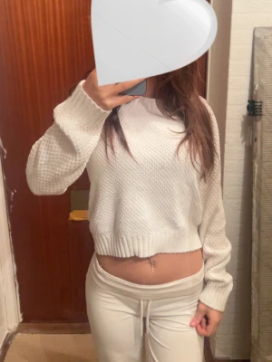 Vit stickad croppad tröja med snörning - Säljer en vit croppad stickad tröja med snygg snörning i ryggen. Tröjan har långärmad passform, ribbade muddar och en cool struktur i materialet. Perfekt för dig som vill ha något trendigt och bekvämt till hösten eller våren. Sen är i storlek S