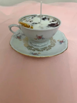 Doftljus i en vit tekopp med blommor i doft utav vanilj nr 4 - Det här ljuset är gjort av återanvändbara material. Tekoppen är köpt secondhand och stearinet är från kyrkor som tänkte slänga det. Det här ljuset har en svag doft utav vanilj, så känsliga även kan använda det. Det här ljuset har även torkade blommor och torkad apelsin på som dekoration. Det finns fler av denna design på hemsidan om man vill köpa sets. 