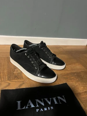Svarta sneakers från Lanvin med lackdetalj - Säljer ett par riktigt feta Lanvin skor! Skorna är svarta med vit sula, riktigt snygga och stilrena skor som jag skulle säga passar till allt! Skicket är väldigt bra skulle jag själv säga men man bedömer självklart skicket ut efter bilderna, baga att skriva vid minsta fundering💫 og endast dustbag som syns på bild! Defekter kan förekomma då det ej är nya så som creesad Skorna är i uk 8 vilket sitter som 42-43.5 skulle jag säga då de är stora i storlek! Självklart äkta och som sagt riktigt snygga🌟