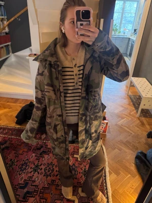 Camouflage jacka från Canada Goose - Säljer en snygg camouflagefärgad jacka från Canada Goose. Jackan har huva, flera fickor och klassisk patch på ärmen. Materialet är slitstarkt och jackan har en loose passform.