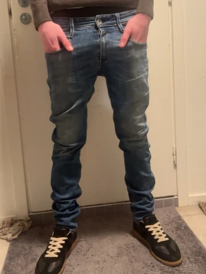 Replay Anbass blå jeans, storlek 30/32 - Säljer ett par Replay Anbass jeans i klassisk blå tvätt. De har slim passform, normal midja och raka ben. Jeansen är tillverkade i mjukt denimtyg och har snygga slitningar framtill. Perfekta för dig som gillar en clean men ändå avslappnad look.