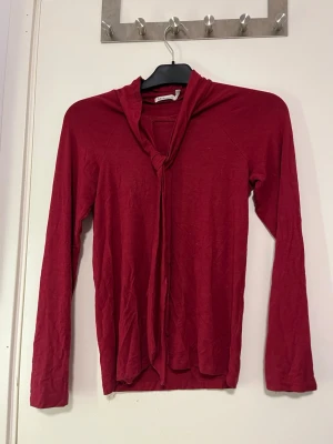 Röd långärmad tröja med knyt - Säljer en röd långärmad tröja från Mira Selected i storlek XS. Tröjan har ett snyggt knyt framtill vid halsen som man kan justera hur man vill och är tillverkad i ett mjukt, tunt material. Perfekt för dig som gillar enkel men ändå unik stil. Väldigt skönt material. Använd fåtal gånger. Pris kan alltid diskuteras!🤗