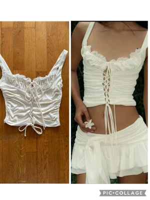 Vit korsett-topp med spets och snörning M - Säljer en vit korsett-topp med breda axelband, snygg snörning framtill och romantisk spetskant vid urringningen. Toppen är croppad och har en omlottkänsla med rynkade detaljer. Materialet är mjukt och stretchigt, troligen polyester eller bomull.