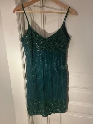 Grön pärlbroderad kortklänning Castelbajac - Supersnygg grön kortklänning från Castelbajac med tunna axelband och detaljerat pärlbroderi i cirkelmönster upptill och nedtill. Klänningen har smal passform och är täckt av små pärlor som ger en glittrig effekt. 