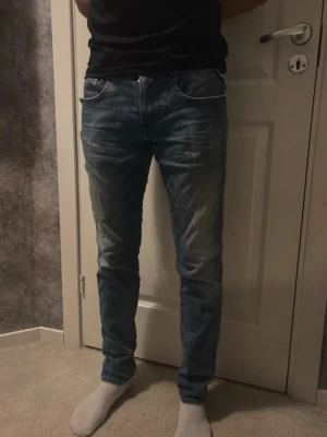 Replay Hyperflex blå jeans - Säljer ett par Replay Hyperflex jeans i blå tvätt med snygga slitningar och klassiska fem fickor. Jeansen har normal passform och är tillverkade i stretchigt jeansmaterial för extra komfort. Märkespatch bak i midjan och coola detaljer vid bakfickorna. Storlek W30