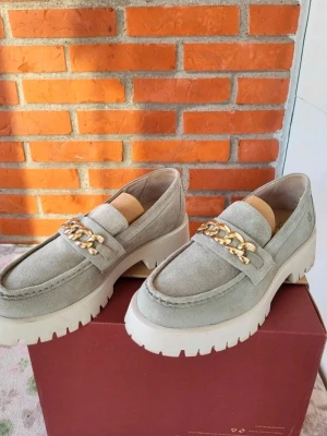 Rosa Negra Loafers, mint grön läder guld detaljer, Storlek 40 - Snygga beige loafers i mocka med chunky vit sula och en fet guldfärgad kedjedetalj över foten. Skorna har rund tå och grov platt sula som ger en cool look. Perfekta för dig som vill ha något trendigt och bekvämt till vardags.