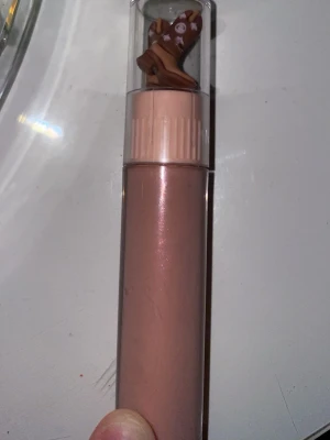 Nude läppglans med söt dekor - Läppglans i en nude-rosa nyans med glansig finish. Förpackningen har ett genomskinligt lock med en gullig dekor av bruna vantar med små vita detaljer. Perfekt för dig som gillar söta detaljer på sminket.