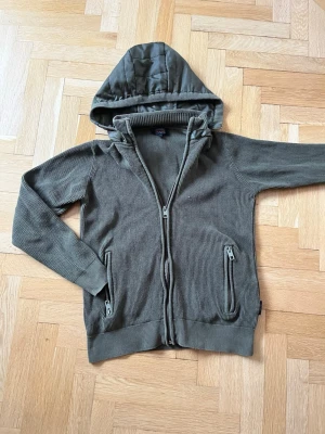 Sälsynt’ indicode cardigan - Säljer den eftertraktade olivgröna ribbade cardiganen av indicode jeans, med avtagbarluva, schysst passform och en tidlös färgning, perfekt till alla säsonger. Kan kläs upp samt som ned. 