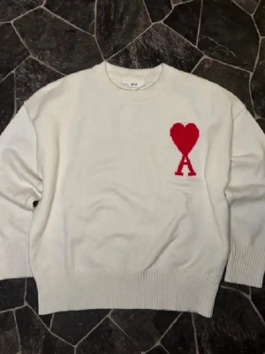 Vit stickad tröja från Ami Paris - Säljer en vit stickad tröja från Ami Paris med röd hjärtdetalj och stort A på bröstet. Tröjan har rund halsringning, ribbade muddar och lång ärm. Perfekt för dig som vill ha en clean men ändå statement look. Priset kan diskuteras vid snabbaffär