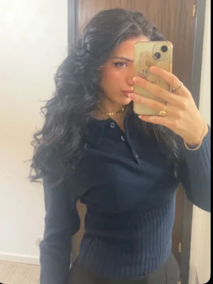 Mörkblå stickad polotröja - Säljer en mörkblå stickad polotröja med krage och knappar framtill. Tröjan har lång ärm och ribbad midja som ger en snygg passform. Perfekt för dig som gillar klassisk och stilren look.