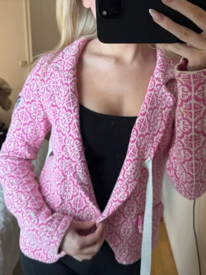 Rosa mönstrad kofta från Odd Molly - Supersnygg rosa och vit kofta från Odd Molly med broderad patch på ärmen och ett unikt mönster över hela plagget. Koftan har lång ärm, krage och knytband i midjan för extra detalj. Perfekt för dig som vill sticka ut lite extra!
