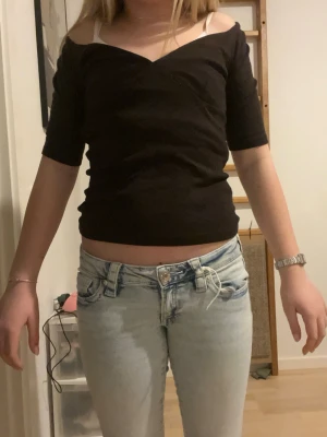 Mörk brun omlottopp från Zara - Säljer en mörk brun omlottopp från Zara med v-ringad hals och halvlånga ärmar. Toppen har en offshoulder-look och sitter tight mot kroppen. Perfekt för dig som gillar stilrena och enkla plagg med en twist.