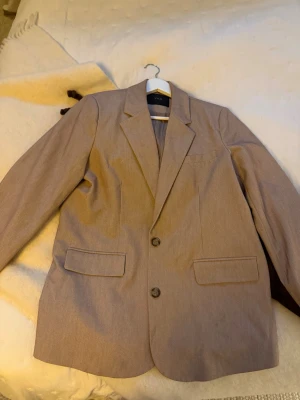 Beige kavaj från YAS med klassisk look - Säljer en beige kavaj från YAS med klassisk krage, två knappar framtill och fickor med lock. Kavajen har en rak passform och är fodrad på insidan. Perfekt för dig som gillar stilrena och tidlösa plagg.