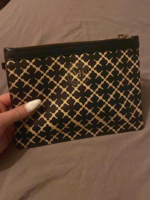 Malene Birger - Snygg kuvertväska från Malene birger i svart och beige med ett grafiskt rutmönster. Väskan har guldfärgad dragkedja och är tillverkad i skinn. Perfekt storlek för mobilen och småsaker, med stilren design och logga framtill.