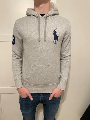 Ralph Lauren Hoodie - Grå Ralph Lauren hoodie med en stor svart ponny logga🐎  Storlek S, men passar även M. Personen på bilden är ca 185cm och väger 75 kg.📏  I mycket fint skick, inga hål eller liknande✨  Priset går såklart att diskutera så kom med förslag😊