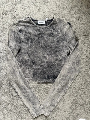 Grå croppad långärmad topp Weekday - Säljer en croppad långärmad topp från Weekday i tvättad grå färg. Toppen har en rund halsringning och är gjord i mjuk bomull. Perfekt till jeans eller kjol för en cool vardagslook.