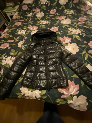 lager 157 jacka - Säljer en svart pufferjacka med glansig yta och huva från lager157. Perfekt för kalla dagar och har en snygg, modern look. den är i storlek xxs och finns inget täcken på användning 