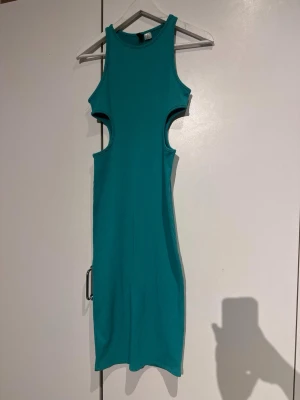Turkos ribbad klänning från DIVIDED - Säljer en turkos ribbad klänning från DIVIDED i storlek S. Klänningen är ärmlös med coola cut-outs vid sidorna och har en slits nedtill. Materialet är mjukt och stretchigt, perfekt för dig som gillar en slim passform och vill sticka ut med färg. Very strechy so can fit to M 