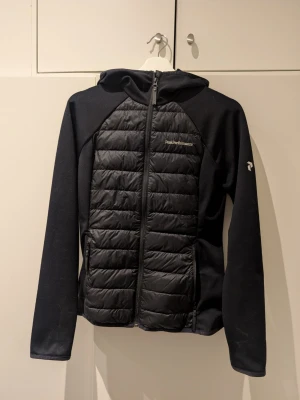 Svart hybridjacka Peak Performance M - Svart hybridjacka från Peak Performance i storlek M. Jackan har quiltade partier framtill och baktill. Modellen heter W Down Hybrid Hood Jacket. Kostade ca 2500 i inköpspris.