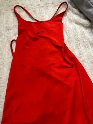Röd tajt långklänning med snörning - Säljer en röd långklänning med tunna axelband och snygg snörning i ryggen. Klänningen har en figurnära passform och är ärmlös, perfekt för dig som vill sticka ut. Materialet känns mjukt och följsamt mot kroppen. S/xs