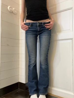Blå bootcut jeans från Junkyard. - Säljer ett par blå bootcut jeans från Junkyard i storlek XS. Jeansen har låg midja, klassisk femficksmodell och snygga kontrastsömmar.