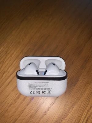 Trådlösa hörlurar med laddningsetui - Snygga vita trådlösa hörlurar med laddningsetui i läderliknande material. Hörlurarna har modern design och laddas via USB. Passar perfekt för musik och samtal på språng. Inga synliga skador eller slitage, ser ut att vara i gott skick.