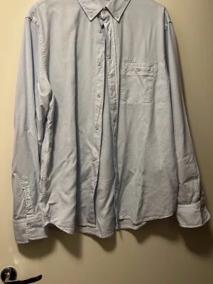 Ljusblå skjorta från Filippa K - Snygg ljusblå skjorta från Filippa K med klassisk krage och bröstficka. Skjortan har långa ärmar med knappar vid manschetten och är tillverkad i mjuk bomull. Perfekt för dig som gillar stilrena och enkla plagg. Aldrig använd passar mig ej