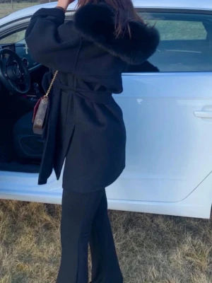 Svart kappa med pälsdetalj och bälte - Kappa med äkta päls – bellojackets  Svart kappa i mycket fint skick, endast använd vid några tillfällen. Pälsen på kragen är äkta och avtagbar.  Observera: en knapp till pälskragen har lossnat. Pälskragen är därför tillfälligt fastsydd, men det går enkelt att ta bort tråden och sätta dit en ny knapp om man önskar.  Storlek: XS (34) Färg: Svart Skick: Mycket bra  1500kr inklusive frakt 🚚 🌸