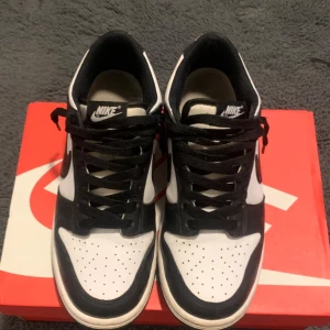 Nike Dunk Low svart/vit sneakers - Nike Dunk Low sneakers i svart och vitt skinn med klassisk Swoosh på sidorna. Lågt skaft, svart snörning och vit mellansula. Perfekt för dig som gillar stilrena och ikoniska sneakers med streetkänsla.