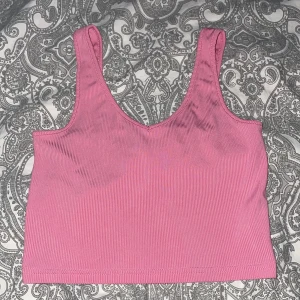 Rosa ribbad linnetopp från SHEIN - Säljer en rosa ribbad linnetopp från SHEIN i storlek S. Toppen är croppad med breda axelband och har en enkel, stilren design. Perfekt för att matcha med jeans eller kjol. Materialet är stretchigt och  är som tränings material typ. Säljer den då jag fick den av en kompis men de blev att jag aldrig använde den💗