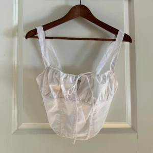 Vit korsett-topp från Bershka - Säljer en vit korsett-topp från Bershka med breda axelband och snygg knytning framtill. 🤍