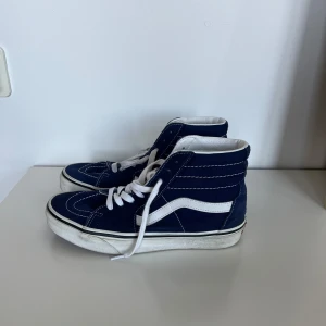 Blåa Vans Sk8-Hi sneakers - Säljer ett par klassiska Vans Sk8-Hi sneakers i marinblå mocka och canvas med vita detaljer och snörning. Skorna har hög modell, vit sula. Använda ett fåtal gånger och därav i bra skick. 