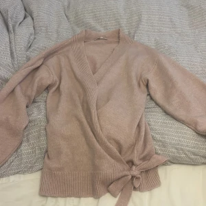 Rosa omlottkofta från Noppies - Mysig rosa omlottkofta från Noppies i stickat material. Koftan har v-ringning, långa ärmar och knytband i midjan. Perfekt för lager-på-lager och ger en chill men ändå snygg vibe.