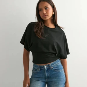 Svart topp från Nelly - Svart croppad topp med rund halsringning och vida, korta ärmar från Nelly. Toppen har en tightare passform över midjan och är tillverkad i ett mjukt bomullsliknande material. Enkel och stilren design som passar till jeans eller kjol.  Den passar perfekt både till vardag som till fest. Den är aldrig använd utan endast provad och är som ny. Säljer då den inte kommer till användning💕