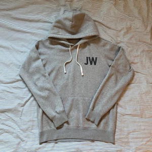 Asnygg Hoodie🙏 - Grå hoodie från Jack Wills med svart JW-tryck fram och stor text på ryggen. Klassisk känguruficka, vita snören i huvan och mjukt material. Perfekt för chill eller träning. Snygg och enkel stil med sportig vibe.