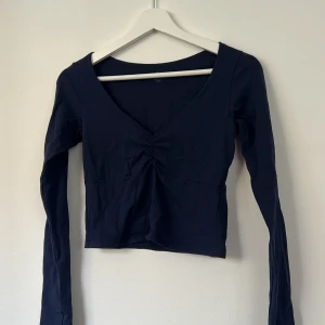 Mörkblå långärmad topp Brandy Melville - Snygg mörkblå långärmad topp från Brandy Melville med v-ringning och rynkdetalj framtill. Modellen är croppad och har en figurnära passform. Tillverkad i mjuk bomull med lite stretch för extra komfort.