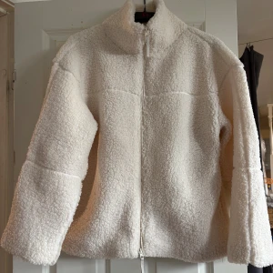 Beige teddyjacka med dragkedja - Mysig och oversized teddyjacka i beige med hög krage och hel dragkedja framtill. Jackan har lång ärm och är tillverkad i fluffigt teddy-material som ger en cool och avslappnad vibe. Helt ny, säljer då jag vill köpa en mindre storlek! 