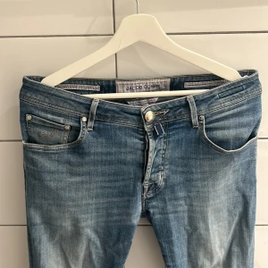  Jacob Cohen - Snygga blå jeans från Jacob Cohen med slitningar och hål på ena knät. Modellen är skinny med klassisk femficksdesign, ljus tvätt och detaljerade sömmar. Perfekta för dig som gillar en avslappnad och trendig look. Storlek 33