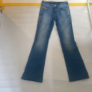 Blå bootcut jeans från Diesel W24 - Snygga ljusblå jeans från Diesel med klassisk femficksdesign och bootcut-ben. Jeansen har en cool tvätt och subtila slitningar, samt Diesel Industry-logga på myntfickan. Perfekta för dig som gillar en avslappnad men trendig look.