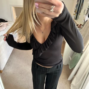 Svart omlottopp med volang - Säljer en svart topp med v-ringning och volanger. Tröjan är ganska använd men de är inget fel på den!